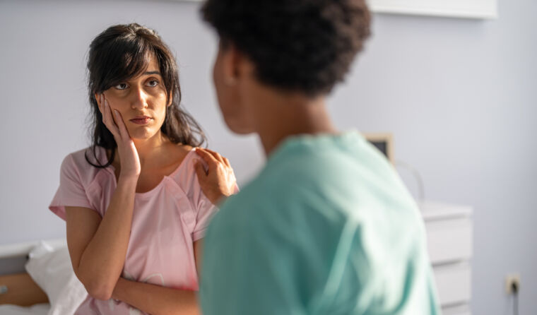 A nurse in blue scrubs speaks to patient in pink