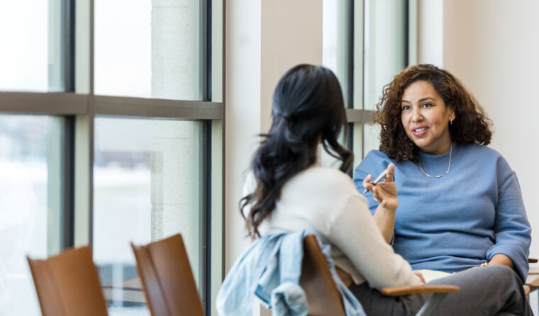 A female GP sits and talks with a female patient.